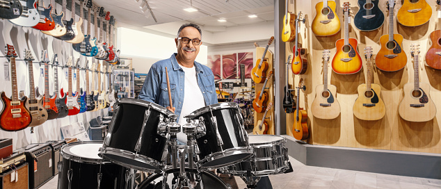 Casual mature man trying drums inside a music shop