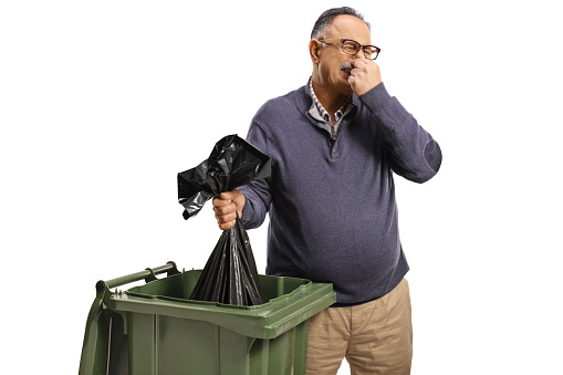 Mature man throwing a smelly bag in a bin isolated on white background