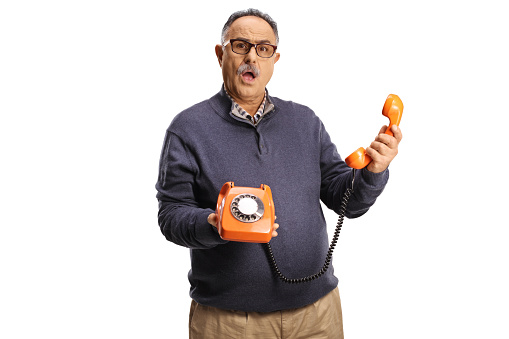 Angry mature man holding a vintage rotary phone and looking at camera isolated on white background