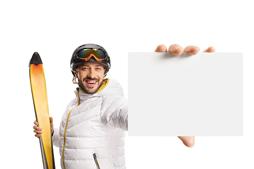 Male skier holding skiis and showing a small blank cardboard isolated on white background