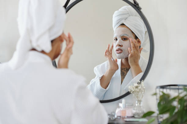 Young woman putting hydrating sheet mask on her face