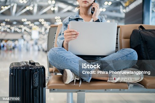 istock Travel vacation concept, asian female woman uses a smartphone and is working on a laptop, she sit wating for flight schedule at terminal airport. 1448711100
