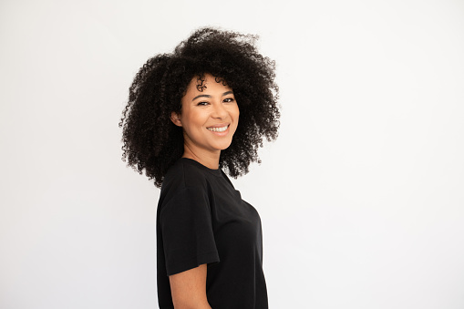 Joyful young woman smiling. Hispanic female model with afro hairstyle and brown eyes in casual clothes smiling from joy standing sideways. Emotion, happiness concept