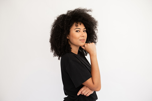 Thoughtful young woman holding thumb on her chin. Caucasian female model with afro hairstyle and brown eyes in black T-shirt standing sideways touching chin with thumb.  Thought, dream concept