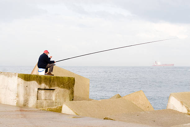 fishing in the levee senior fishing from the concrete blocks of a levee groyne stock pictures, royalty-free photos & images