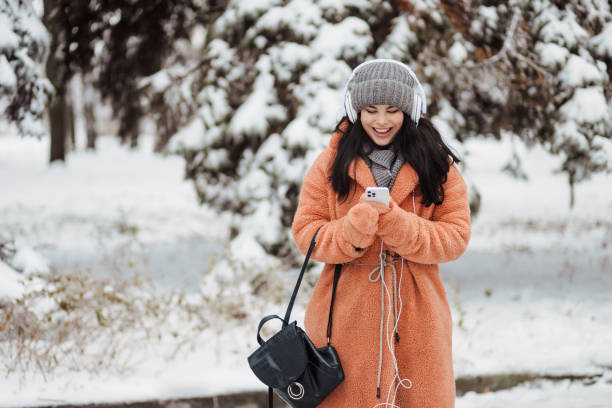 Pretty young long-haired woman in pink coat enjoy winter day and listening music with headphones at snowy park stock photo