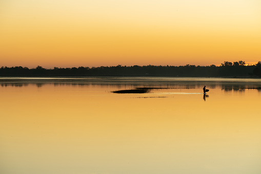 Asian village lifestyle, silhouette of a local Thai male fisherman fishing by a freshwater lake during dawn sunrise time, very beautiful scenic view