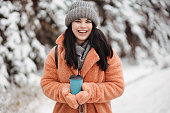 Pretty young long haired woman with amazing smile taking a cup of coffee at a snowy winter park
