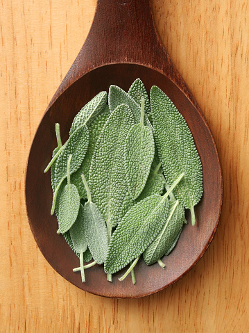 Top view of wooden spoon with fresh sage leaves on it