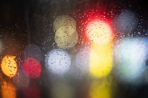Abstract street lights bokeh background and waterdrops on window glass.