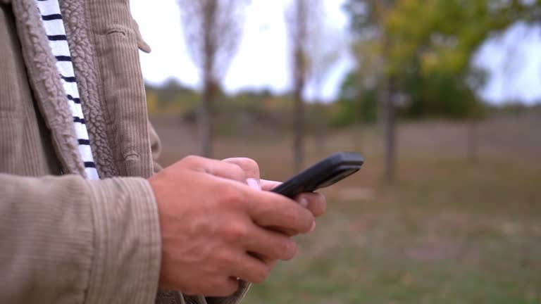 Male hands holding smart phone typing an online message outside in the nature.
