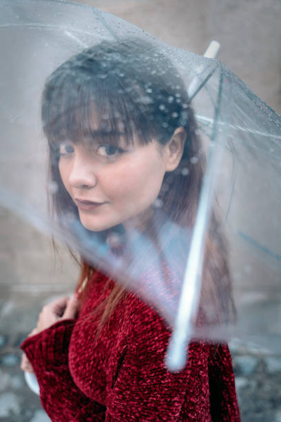 Beautiful woman holding transparent umbrella looking at camera. She is wearing casual clothes.
