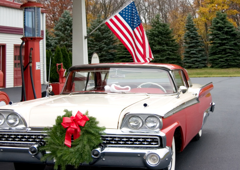 this is a mid 1950s car at a gasoline service station with a wreath on the front of the grill.