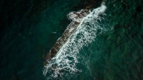 foto aérea de ondas espumosas batendo em uma barreira de pedra - crash barrier - fotografias e filmes do acervo