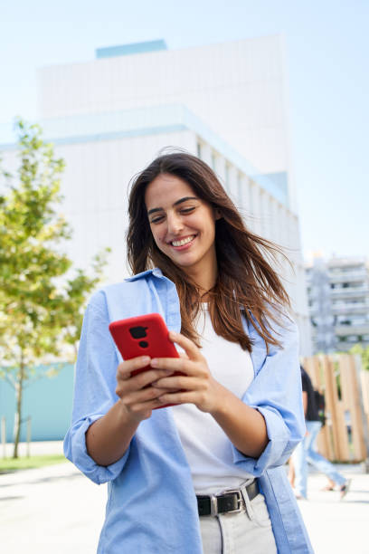 Vertical photo A young girl using a cell phone outdoors. A smiling woman flirting through an app stock photo