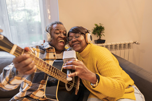 African American senior couple in love spending time together and having fun at home while singing and playing a guitar