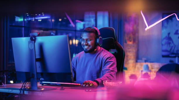 Gaming From Home: Portrait of a Gamer Wearing Headphones and Playing Competitive Video Game on Personal Computer. Professional Stylish Male Player Enjoying Online Multiplayer PvP Tournament. stock photo
