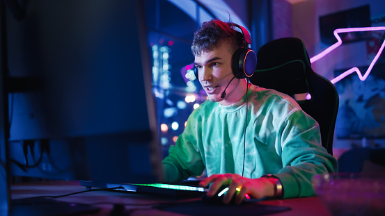 Juegos en casa: Retrato de un jugador con auriculares y jugando en línea en una computadora personal. Jugador masculino profesional con estilo disfrutando del torneo PvP multijugador en línea. photo