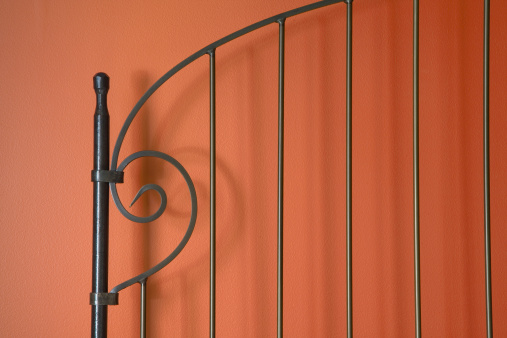 An ornate metal bed frame against a salmon colored wall.
