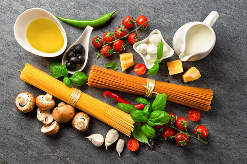 Spaghetti with set ingredients for cooking pasta on a dark stone background, top view