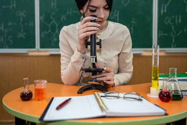 une étudiante pratique dans une classe de chimie avec des flacons sur un tableau avec des formules. - professor adult student chalk drawing formula photos et images de collection