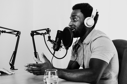 African man recording a podcast using microphone and headphones from his home studio - Black and white editing