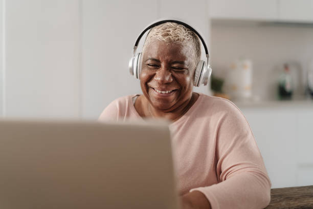 Happy senior woman having fun using a laptop in her house - Technology and smart working concept stock photo