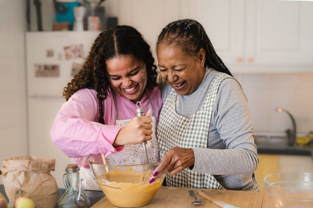 happy african mother and daughter having fun preparing a homemade dessert - grandmother cooking baking family imagens e fotografias de stock