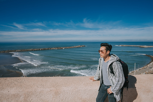 Asian Chinese male tourist looking at North Atlantic Ocean Rabat beach viewing from Kasbah of the Udayas