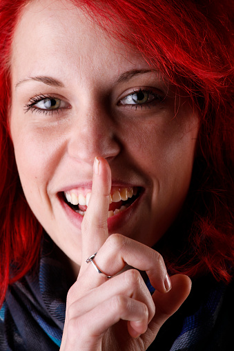 Young woman with finger on lips on black background.