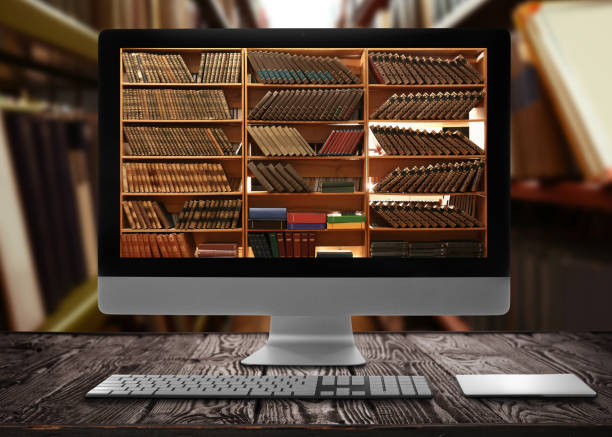Online library. Modern computer on wooden table and shelves with books indoors