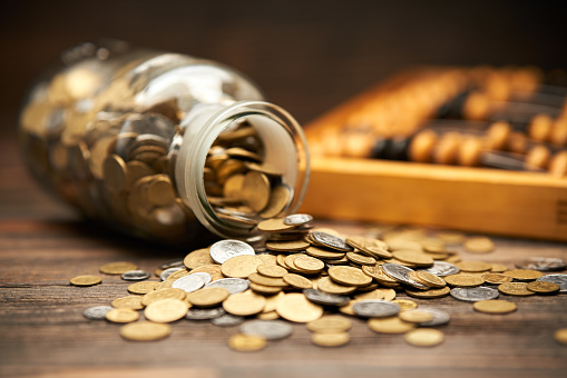 Glass jar filled of golden coins and abacus over wooden background. Money, finance, investment concept