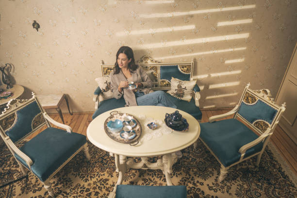 Beautiful young woman sitting in her lovely home on  antique furniture and holding a coffee cup.