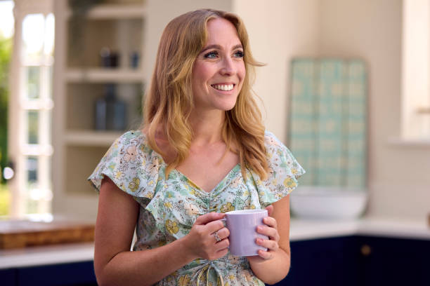 istock Smiling Woman Standing In Kitchen Relaxing With Cup Of Coffee 1448757549