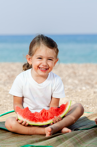 Smiling little girl eating watermelon at the beach