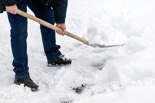 A man cleans snow with a metal shovel