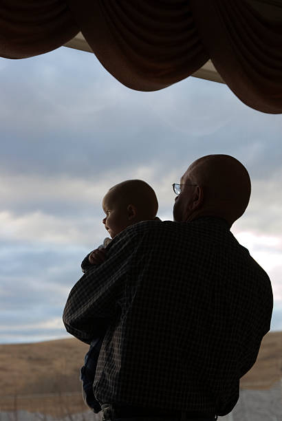 baby and grandfather at window stock photo