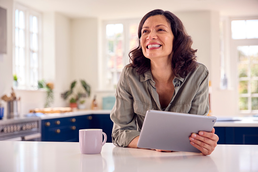 Mature Woman With Using Digital Tablet At Home To Book Holiday Or Shop