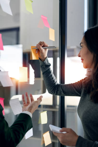 Two young creative team using post it notes in glass wall to writing strategy and business plan.