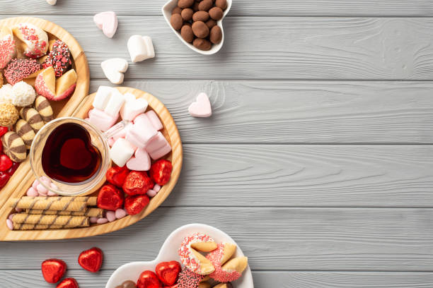 valentine's day concept. top view photo of wooden heart shaped serving tray glass cup of drinking saucers with sweets chocolate jelly candies and cookies on grey wooden desk background with copyspace - valentines day candy chocolate candy heart shape imagens e fotografias de stock