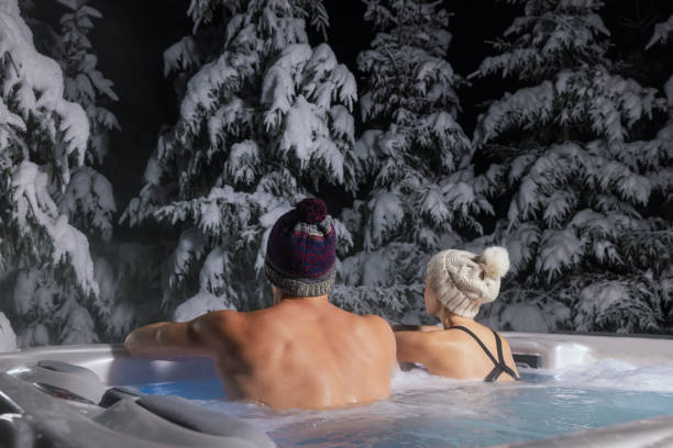 couple relaxing in outdoor hot tub and enjoying snowy winter forest landscape at spa resort stock photo
