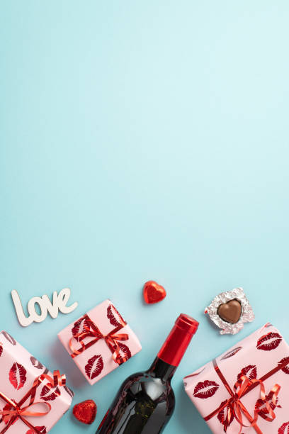 koncepcja walentynkowa. widok z góry pionowe zdjęcie pudełek upominkowych w papierze do pakowania z pocałunkiem usta wzór butelki wina czekoladowe cukierki napis miłość na izolowanym jasnoniebieskim tle z przestrzenią do kopiowania - valentines day candy chocolate candy heart shape zdjęcia i obrazy z banku zdjęć
