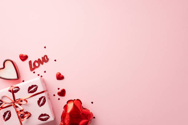 バレンタインデーのコンセプト。パステルピンクの背景に包装紙のギフトボックスのトップビュー写真とキスの唇柄のハート型のキャンドル風船の紙吹雪と碑文の愛とコピー用スペース