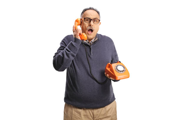 Shocked mature man using a vintage rotary phone and looking at camera isolated on white background