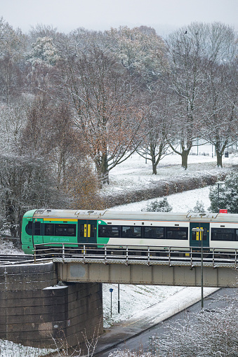 Winter scene depicting a commuter train traveling across a bridge in southeast England in the middle of winter. The town and landscape in the background is covered with a blanket of snow.