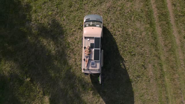 Aerial shot of a man relaxing on the roof of a camper van