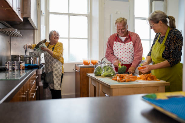 Volunteers Preparing Roast Dinners A shot of volunteers cooking in the kitchen at a warm hub/food bank which is a safe place for people to enjoy a warm and friendly environment in the community with the current cost of living increasing. They are making roast dinners for the visitors. altruism stock pictures, royalty-free photos & images