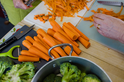 A close-up shot of unrecognisable volunteers peeling vegetables in the kitchen at a warm hub/food bank which is a safe place for people to enjoy a warm and friendly environment in the community with the current cost of living increasing. They are making roast dinners for the visitors.