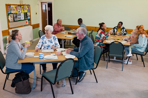 A wide shot of a medium group of people visiting a warm hub/food bank which is a safe place for people to enjoy a warm and friendly environment in the community with the current cost of living increasing. They are waiting for their food to be served.