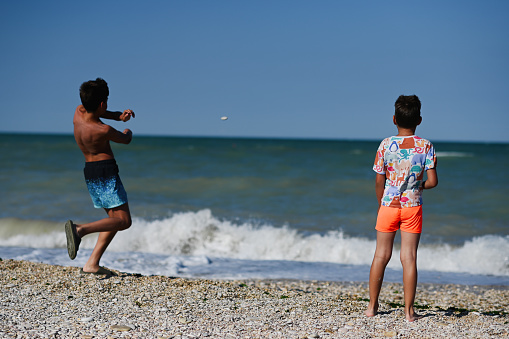 Two brothers throw pebbles into the sea in beach Porto Sant Elpidio, Italy.